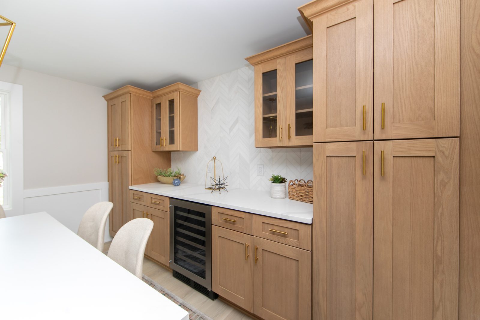 White oak dry bar with glass-front upper cabinets, a herringbone tile backsplash, quartz counter and built-in wine fridge