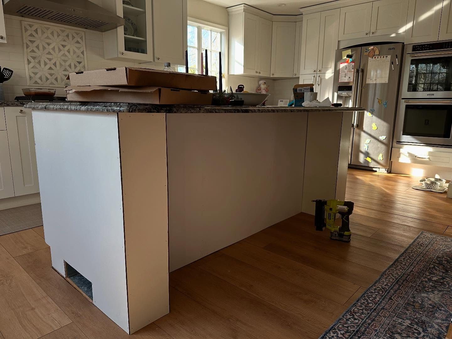 Kitchen island under construction with cream cabinetry and a granite top being fitted