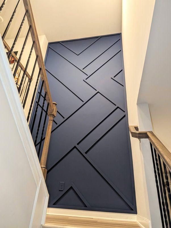 Navy geometric slat accent wall running the full height of a stairwell beside an iron balustrade