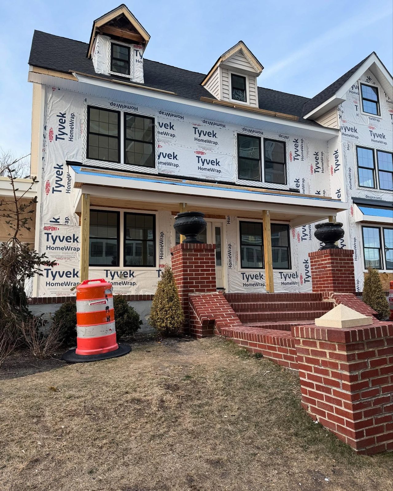 Three-story home mid-renovation with house wrap, new black-framed windows and rebuilt brick porch piers