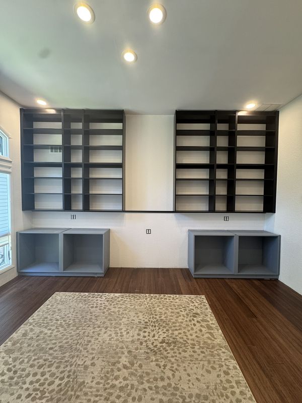 Wall of black built-in bookshelves above pale grey cubby bases, on dark hardwood floors