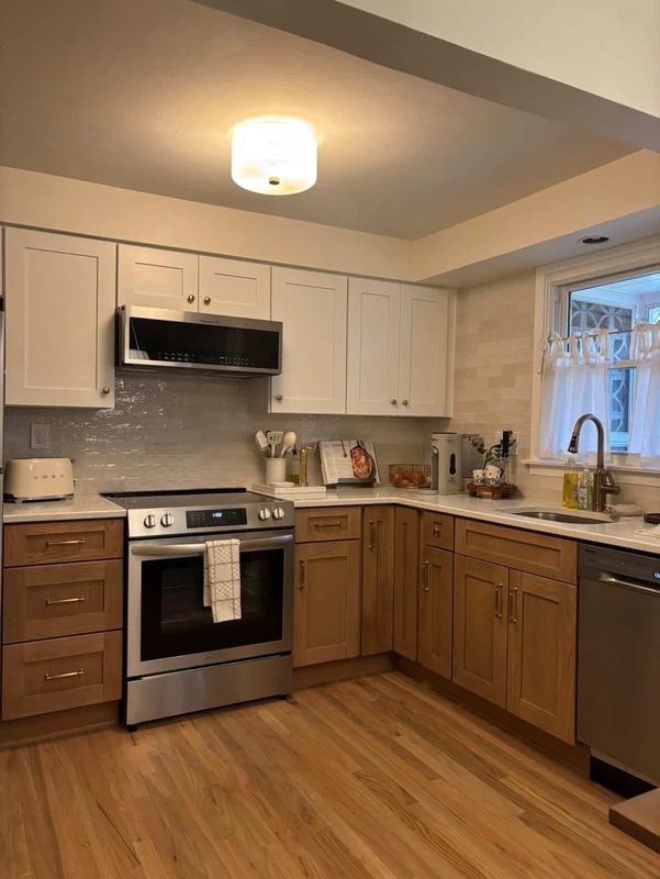Finished kitchen with white upper cabinets, stained oak bases, quartz counters and a glass tile backsplash