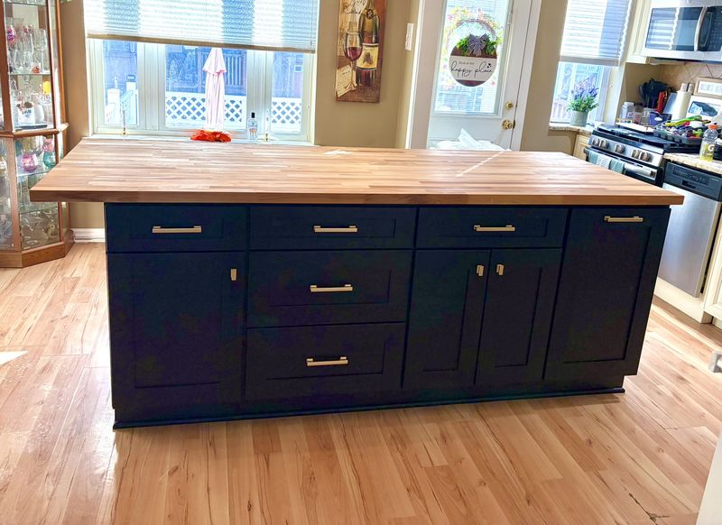 Navy shaker kitchen island with brass bar pulls and a thick butcher-block top, on refinished oak floors