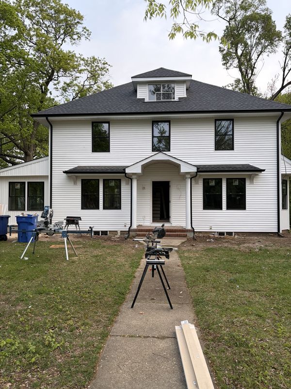 Two-storey white house nearing completion, with black-framed windows and a columned entry portico