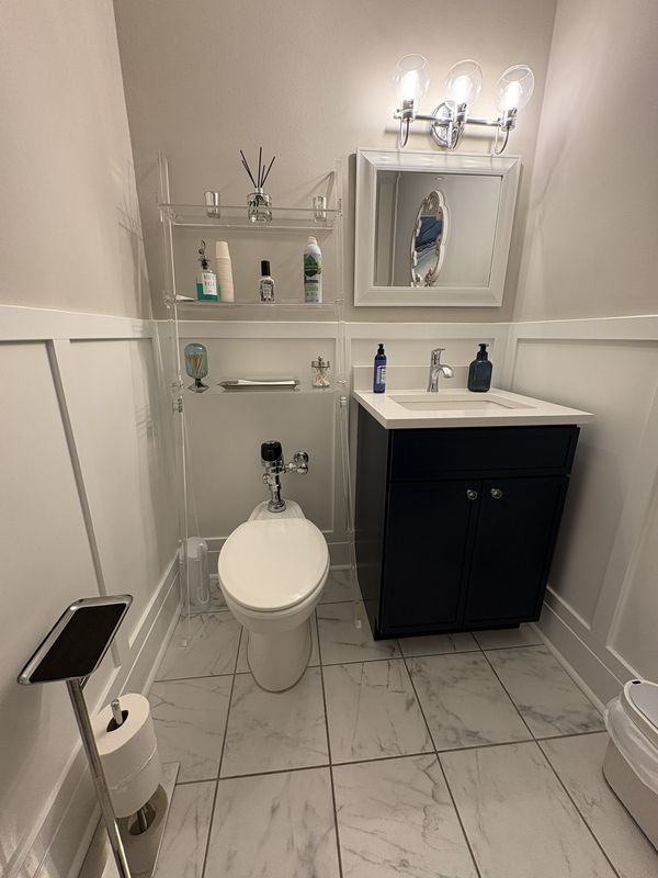 Powder room with white board and batten wainscoting, a navy vanity and marble-look floor tile