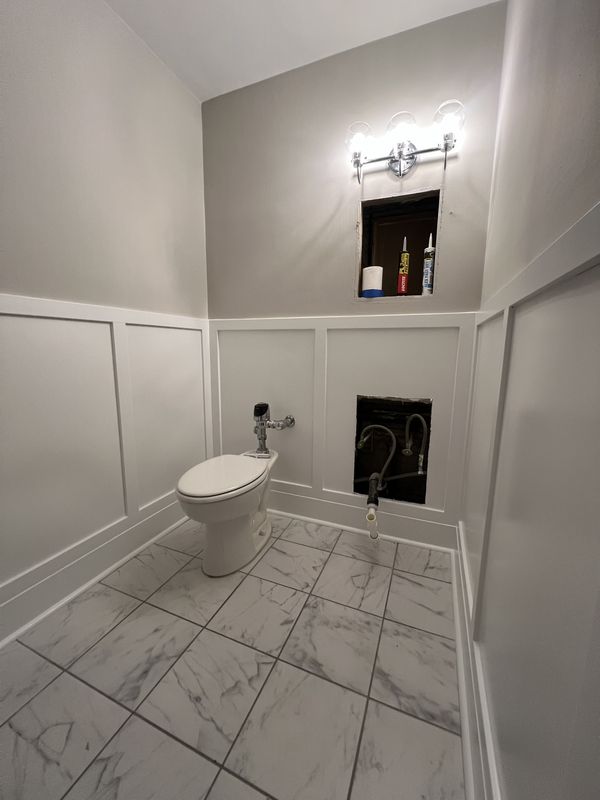 Powder room with tall panel-moulded wainscoting, a recessed niche and marble-look floor tile