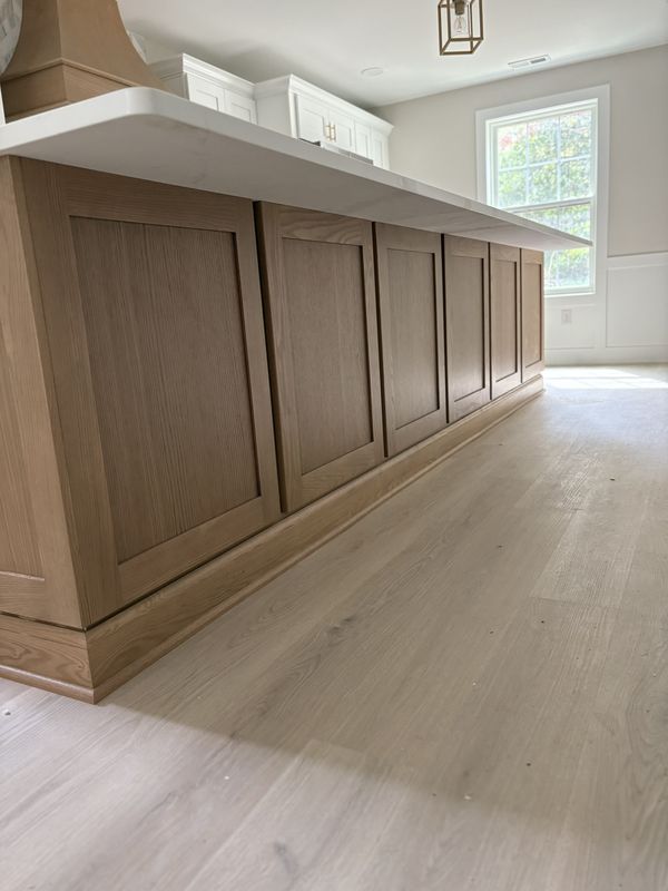 Long stained oak island with recessed panel sides and an overhanging quartz counter, on pale white oak floors