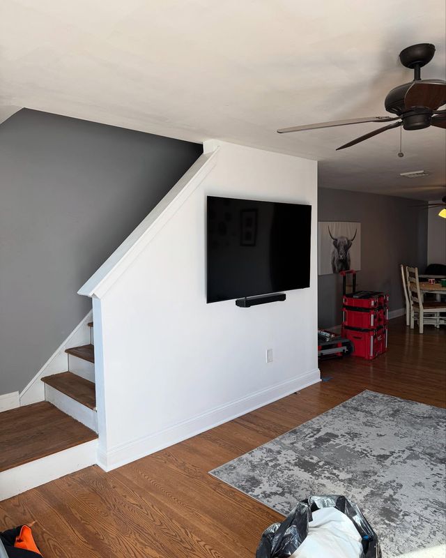 Living room with a grey accent wall, crisp white stair skirt and stringer, and fresh baseboard over hardwood