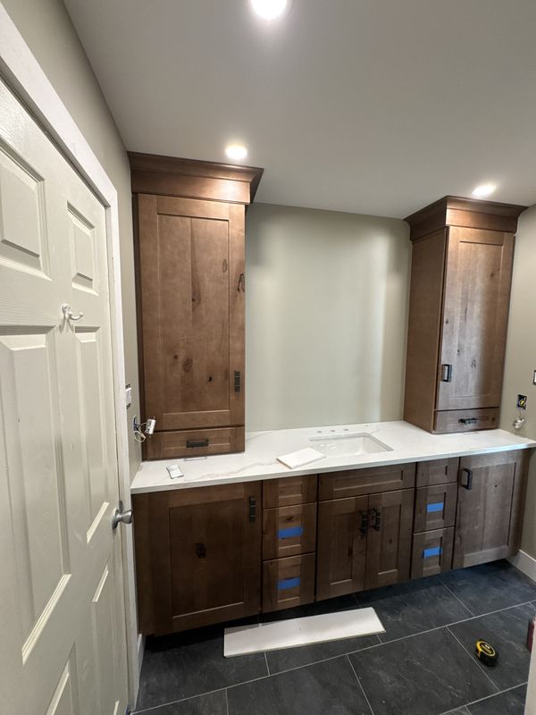 Rustic stained double vanity with matching full-height storage towers and a quartz top, on slate tile