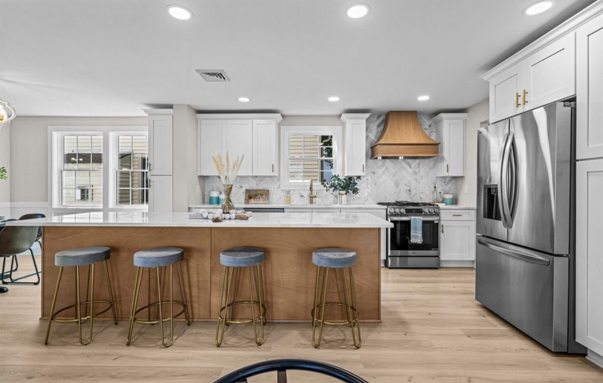 Renovated kitchen with white perimeter cabinets, a wood-clad range hood and a large oak island with upholstered stools